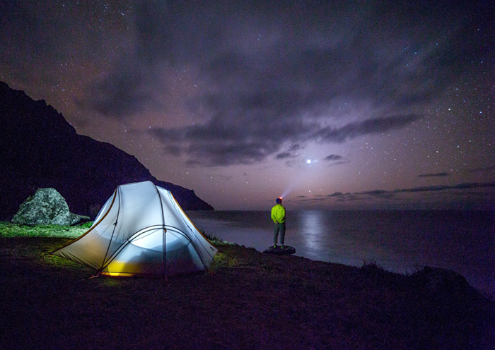 海辺のキャンプサイトから夜空を見上げる旅人