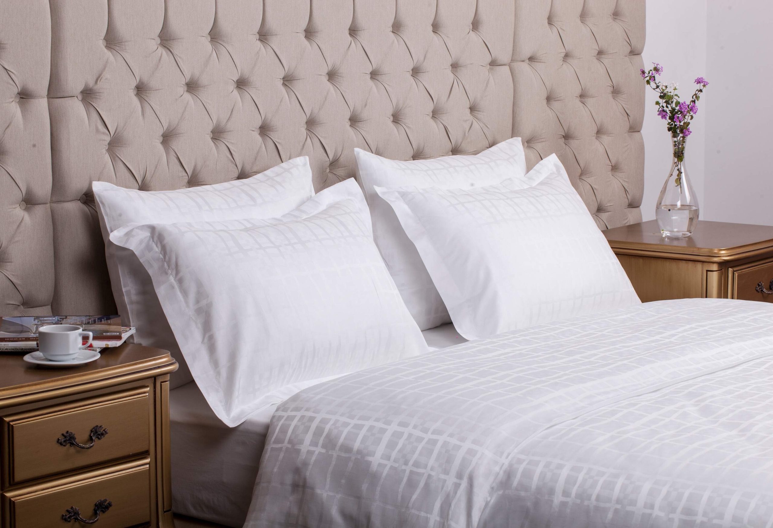 Small golden tables on both sides of the white bed and four pillows leaning against the tufted headboard.